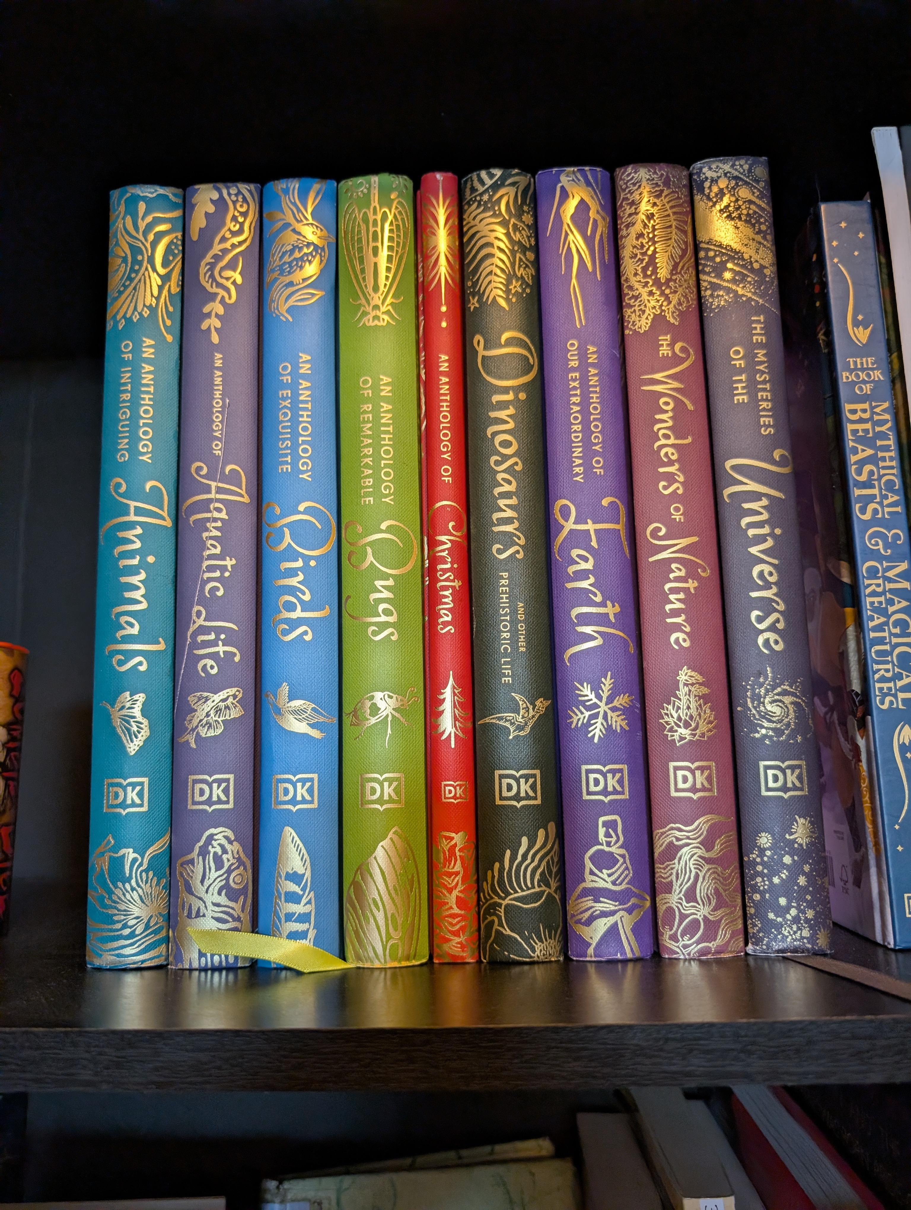 A row of gold-embossed DK anthology books covering animals, aquatic life, birds, bugs, dinosaurs, earth, nature, and the universe